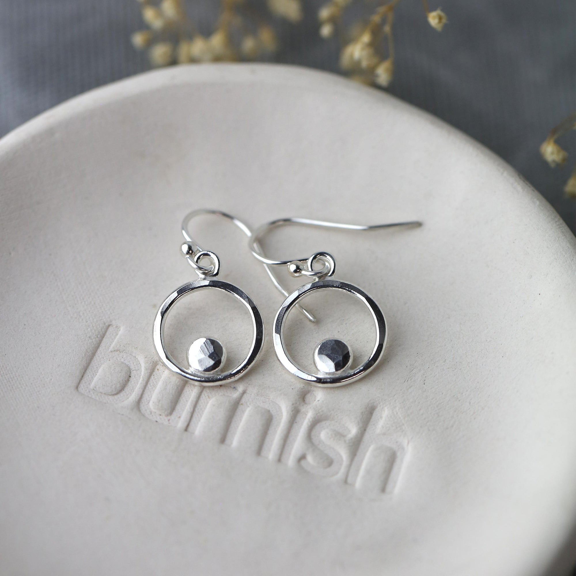 Silver earrings on a white surface with 'Blimish' branding.