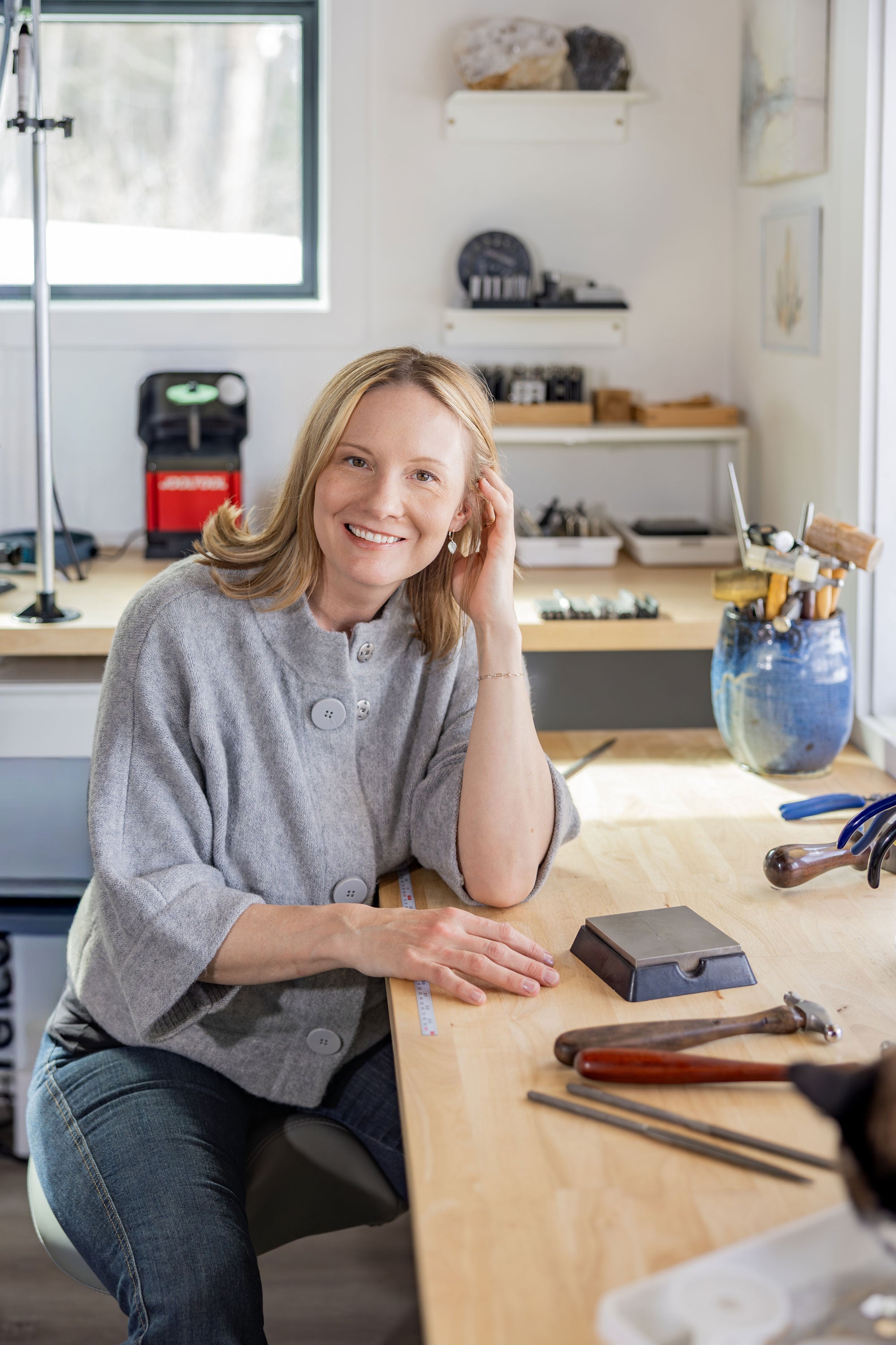 Rebekah sitting at a workbench with tools, smiling in a workshop setting