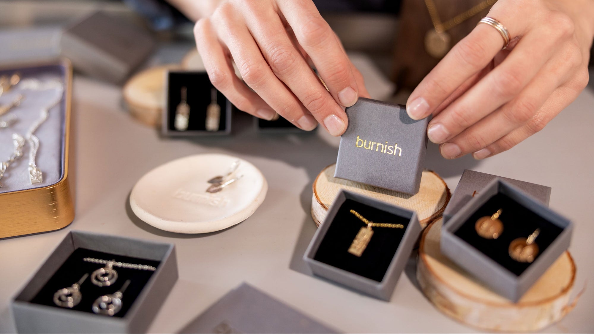 Person holding a jewelry box with 'bournish' branding, surrounded by other jewelry items on a table.